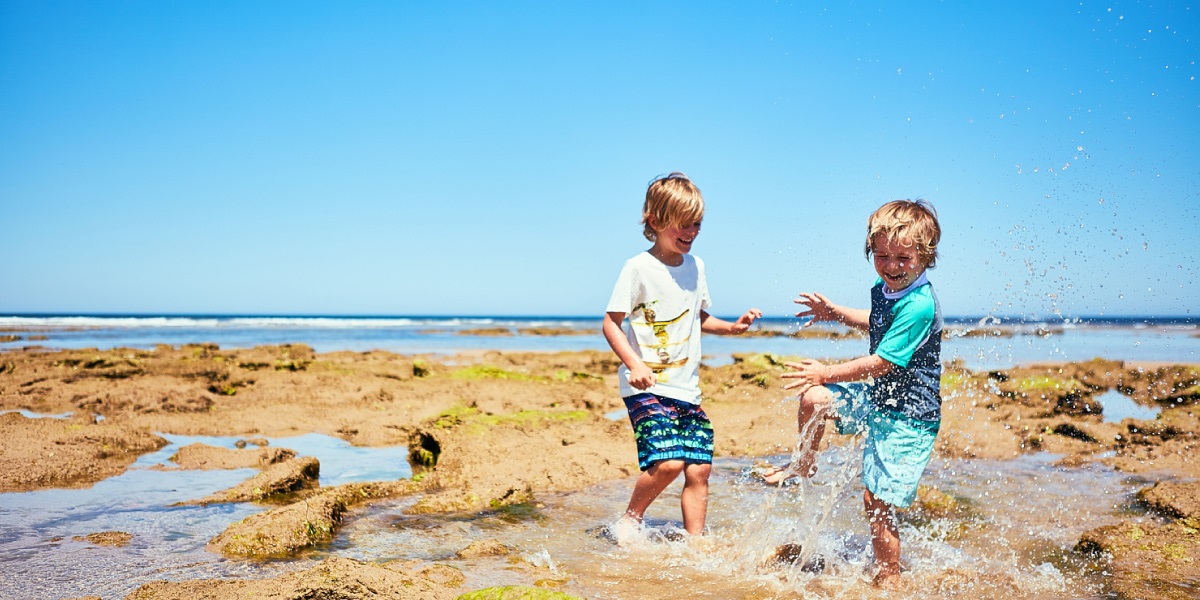Two children playing in the rock pools, splashing in the water with their feet.
