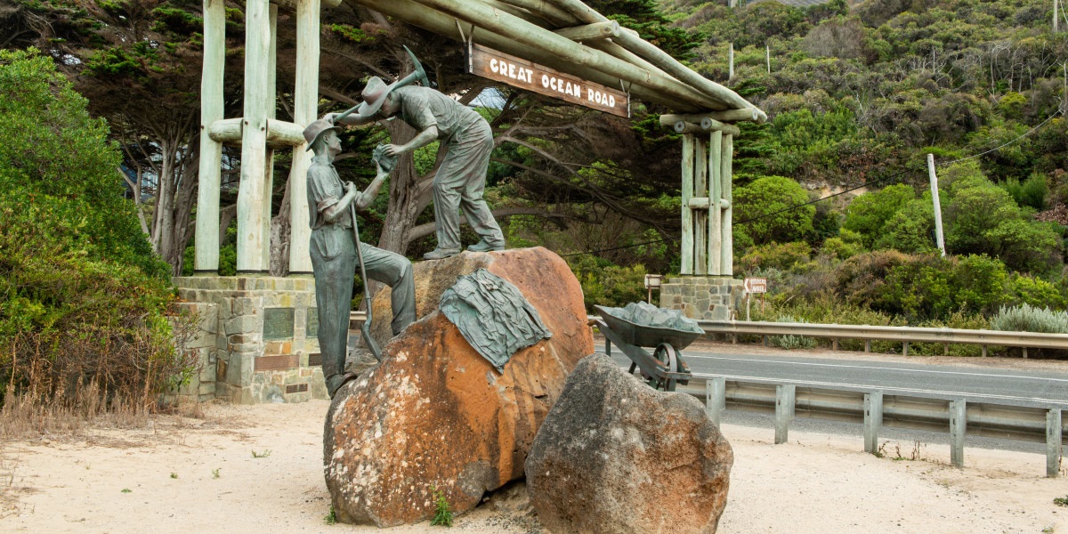 The Great Ocean Road Memorial Arch and digger’s monument, a sculpture of 3 men working on the with picks on a rock with the wooden arch in the background.