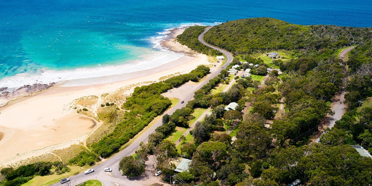 An arial view of Kennett River overlooking the Kennett River Family Caravan Park. The park is framed by the light sandy beach and blue ocean.
