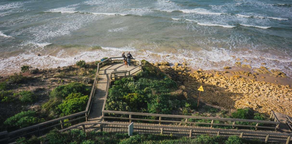 Two people look out to the ocean from a view platform, off the boardwalk along the Torquay shoreline.