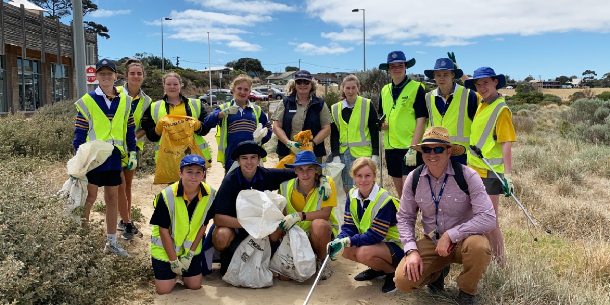 An educator and group of year 9 students in fluorescent vests stand on a beach path after participating, in a beach clean-up. 