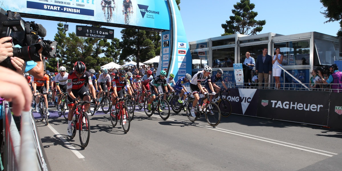 A group of cyclists cross the finish line of a road race.