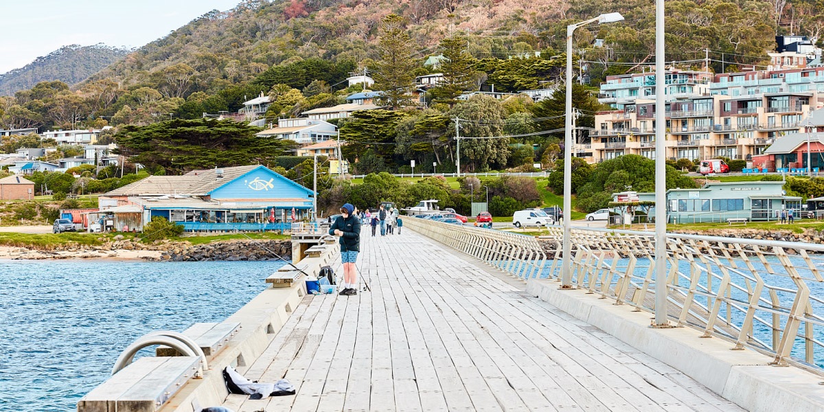 A person fishing on Lorne Pier, in the background you can see the Fishing Co-op and the Lorne hills.