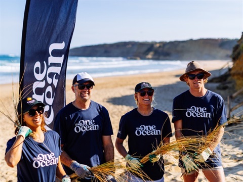 Sally Fitzgibbons (WSL), Luke Hines (Jan Juc Coastal Action), Lakey Peterson (WSL) and Scott Hines (Great Ocean Road Coast and Parks Authority) holding the introduced weed Marram Grass in front of the One Ocean banner.