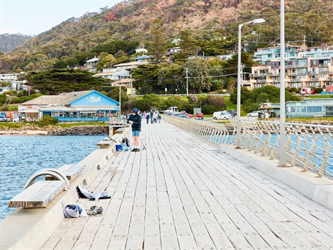 People fishing on Lorne pier with the Fisherman's Co-op and hills in the background.