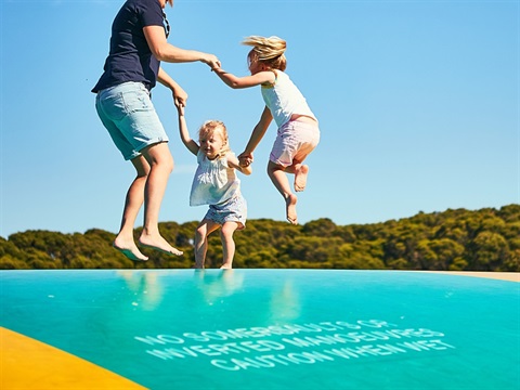 Family holding hands while jumping on a caravan park jumping pillow.